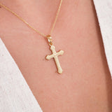 Close-up of an 18K gold vermeil cross necklace for women, resting on the chest over a light V-neck top.