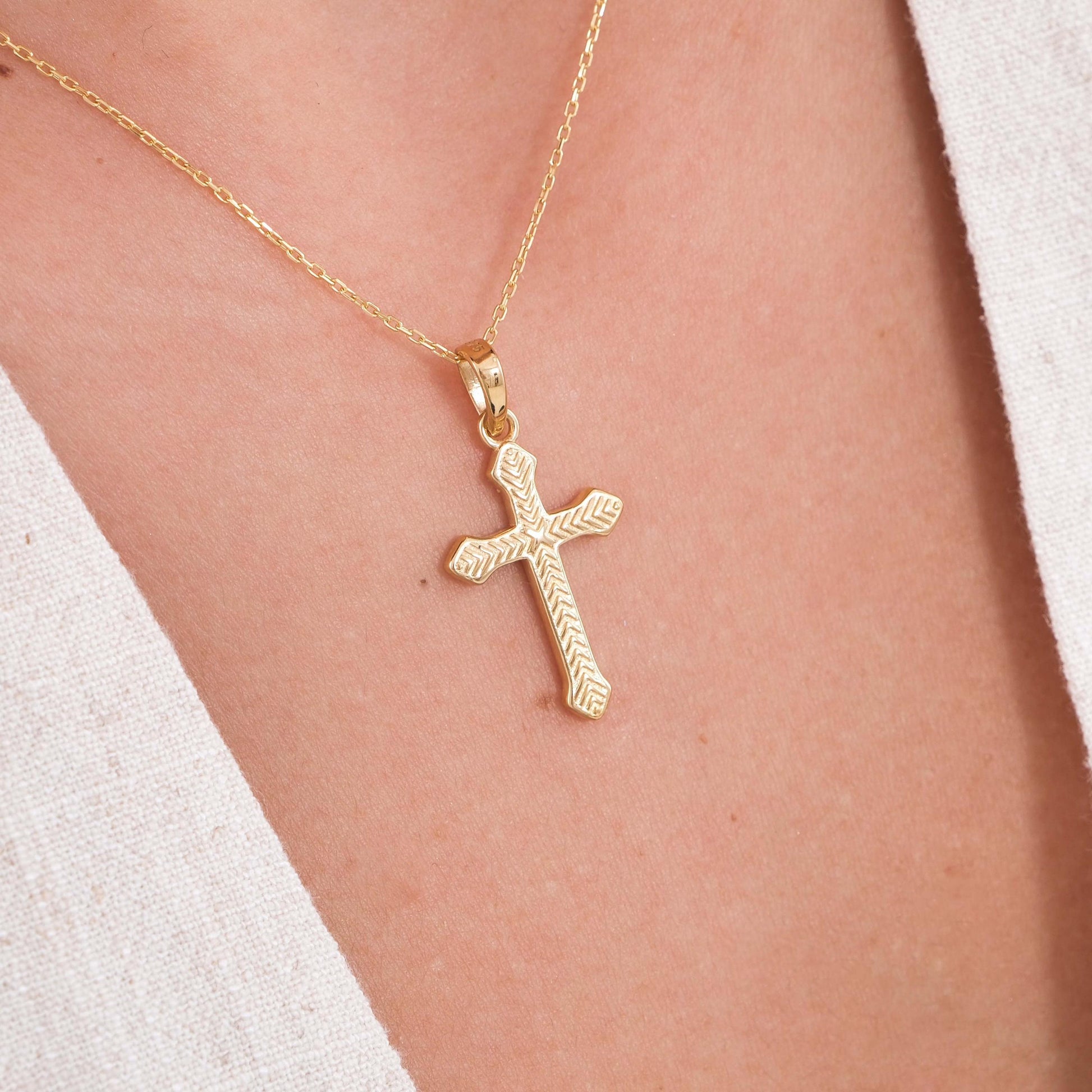 Close-up of an 18K gold vermeil cross necklace for women, resting on the chest over a light V-neck top.
