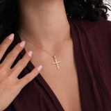 The 18K Gold Vermeil Cross Necklace shown on a woman’s neck with her hand near the pendant.