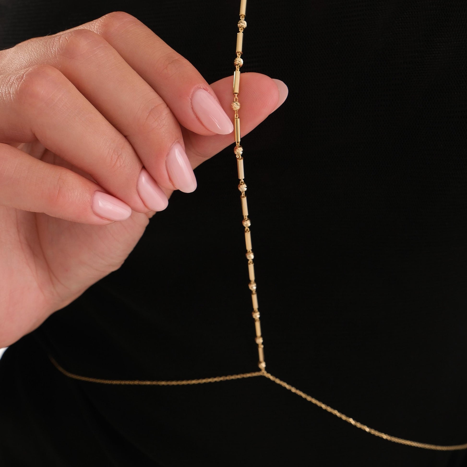 Detailed close-up of the vertical strand of the 18K Gold Vermeil Bar and Bead Body Jewelry held between fingers.