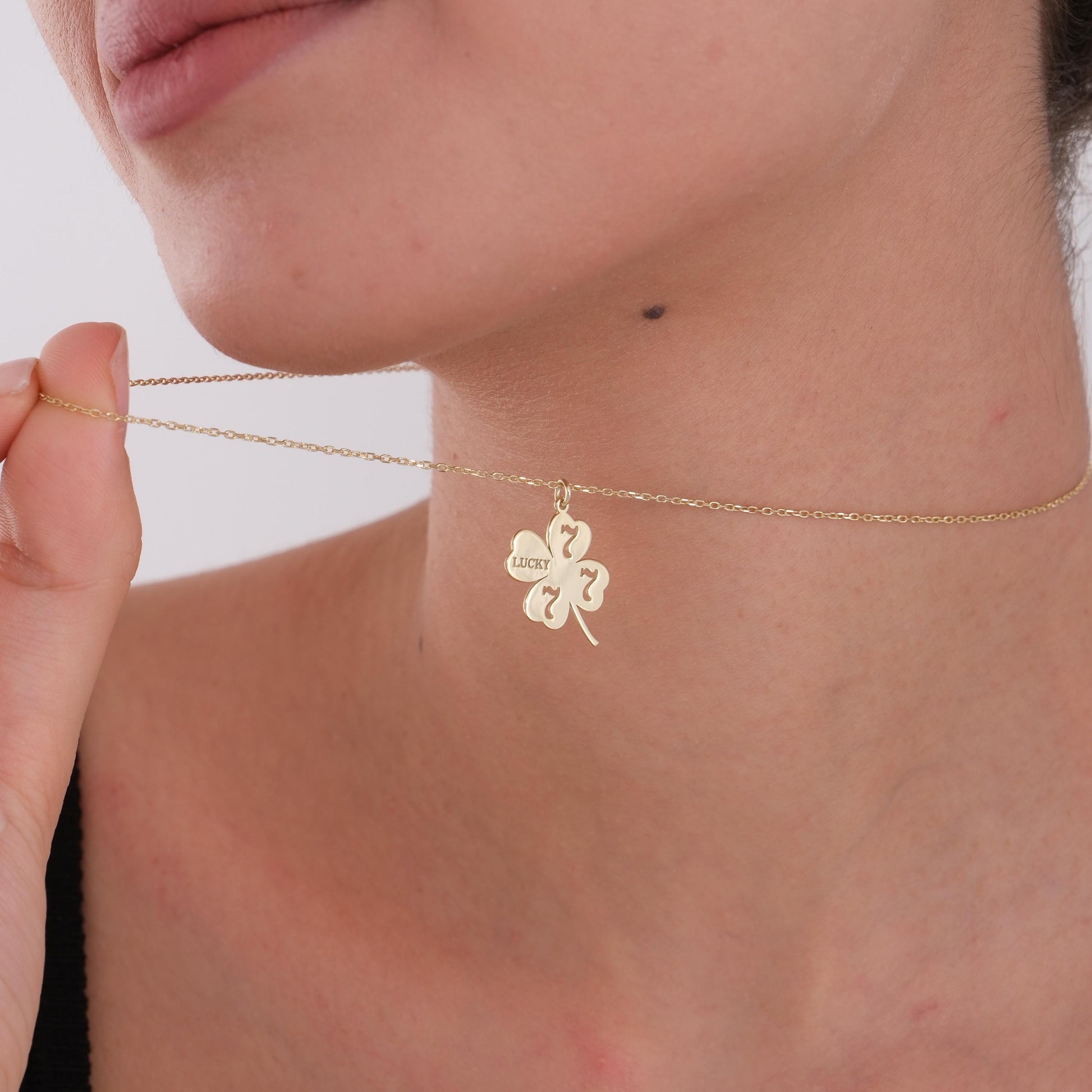 Hand holding the 14K gold lucky clover necklace, highlighting its fine craftsmanship.