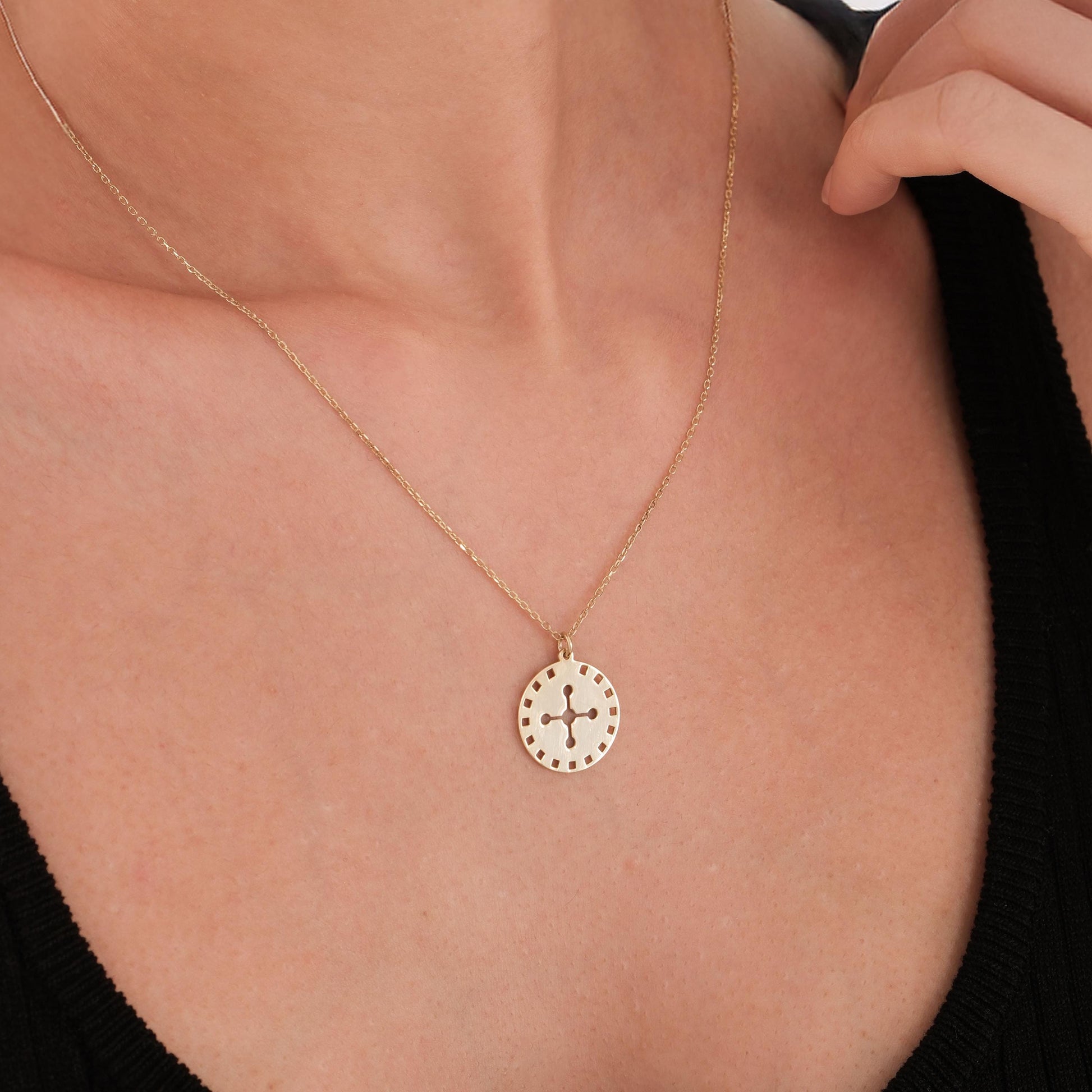 Model wearing a 14K solid gold solar cross necklace layered with other fine gold chains over a white blouse.