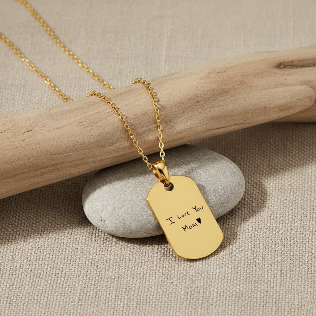 Personalized 18K gold vermeil handwriting necklace with “I love you Mom ♥” engraving on a gold dog tag pendant, styled on a stone and wooden background.