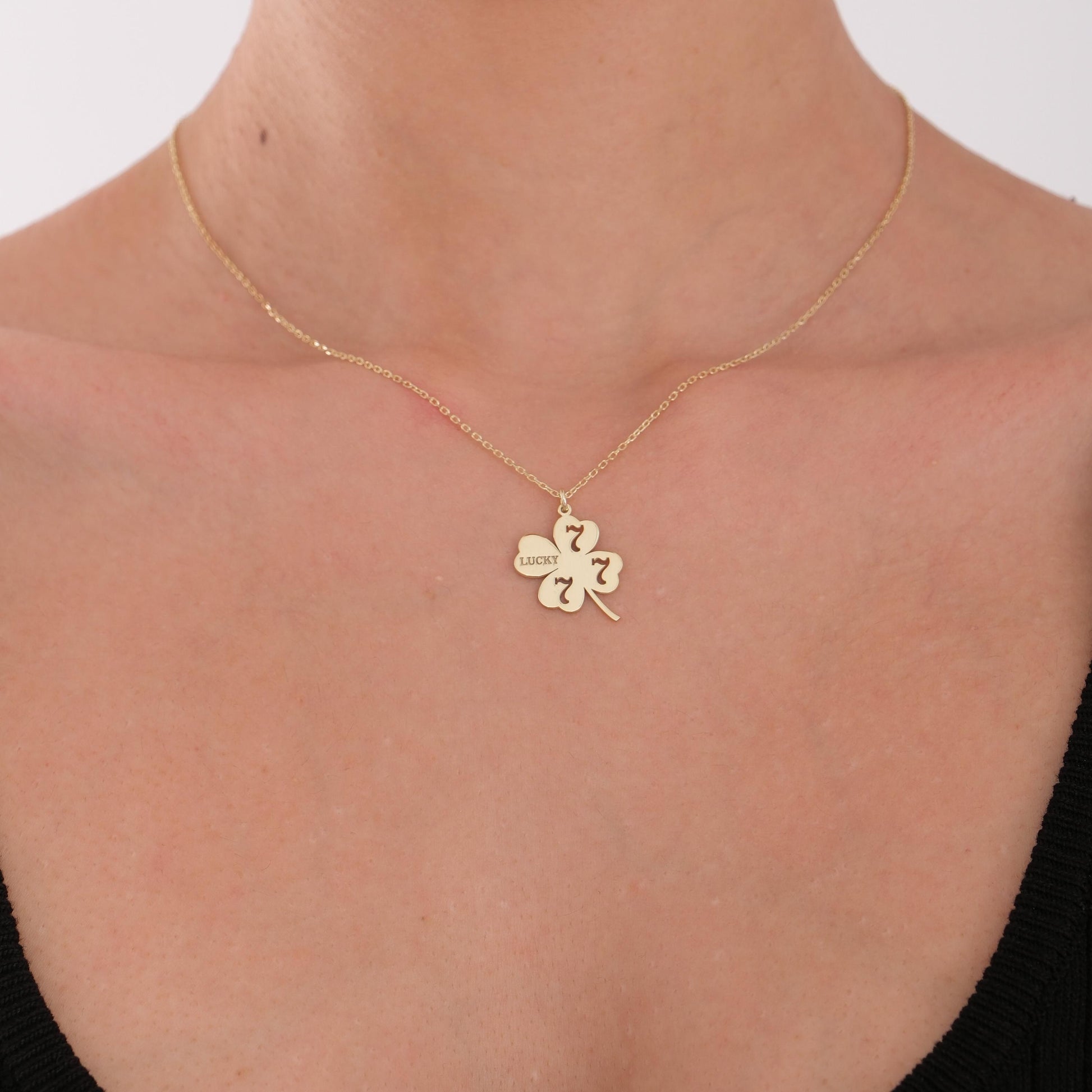 A delicate gold clover necklace featuring “Lucky” and “7” charms, worn elegantly on the neck.