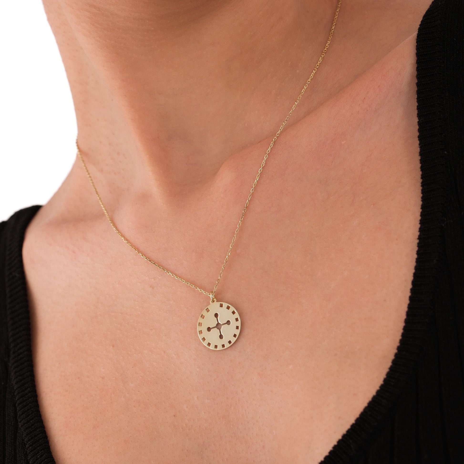 The 14K solid gold solar cross necklace styled with a deep V-neck top, highlighting the pendant’s geometric design.