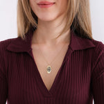 Woman holding her 14K solid gold fingerprint necklace while looking to the side.