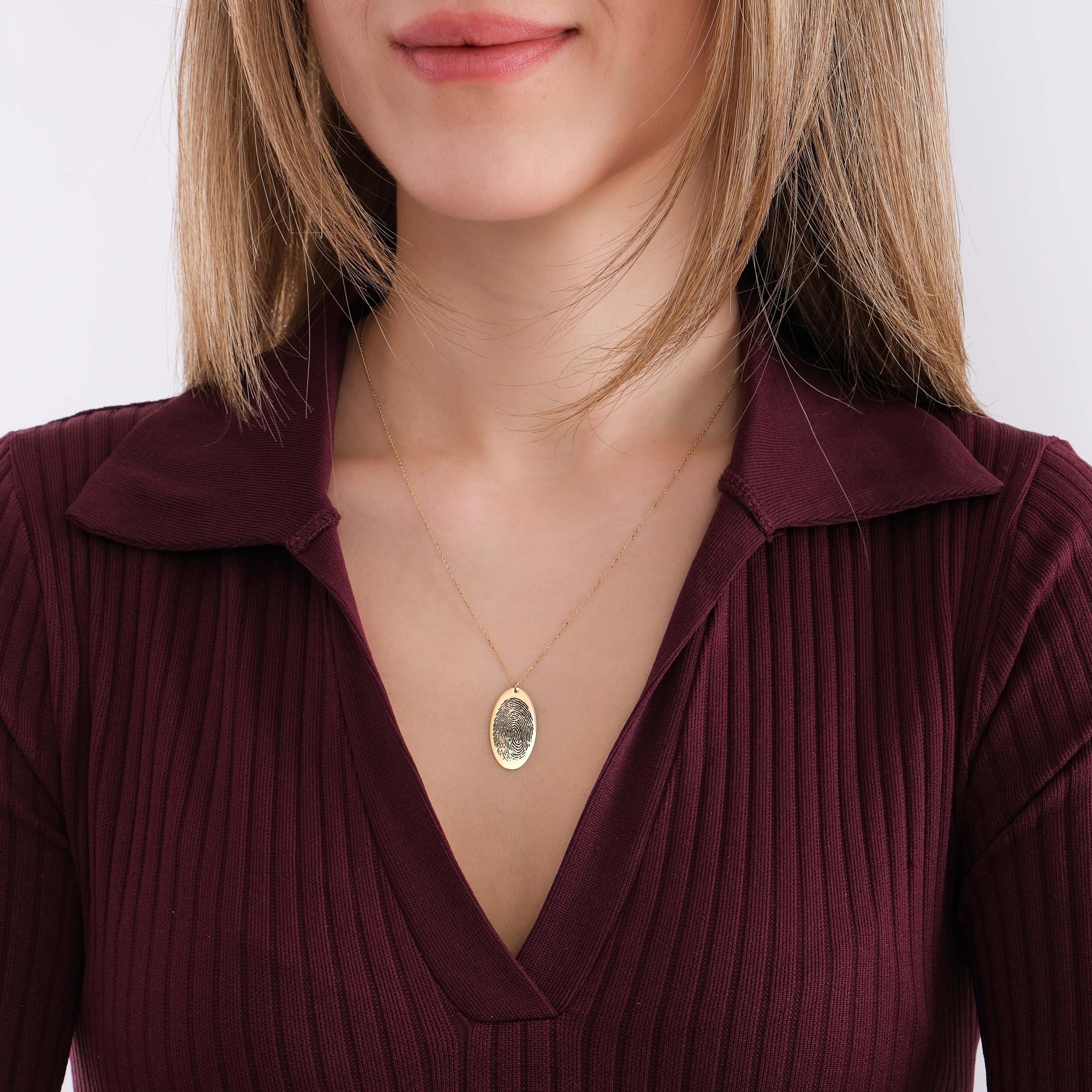 Woman holding her 14K solid gold fingerprint necklace while looking to the side.