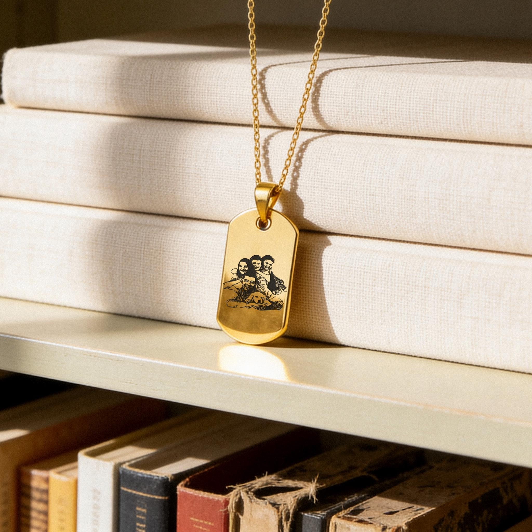 18K Gold Vermeil Custom Picture Necklace featuring a rectangular dog tag pendant engraved with a family portrait, displayed on a gold chain over stacked neutral books on a shelf