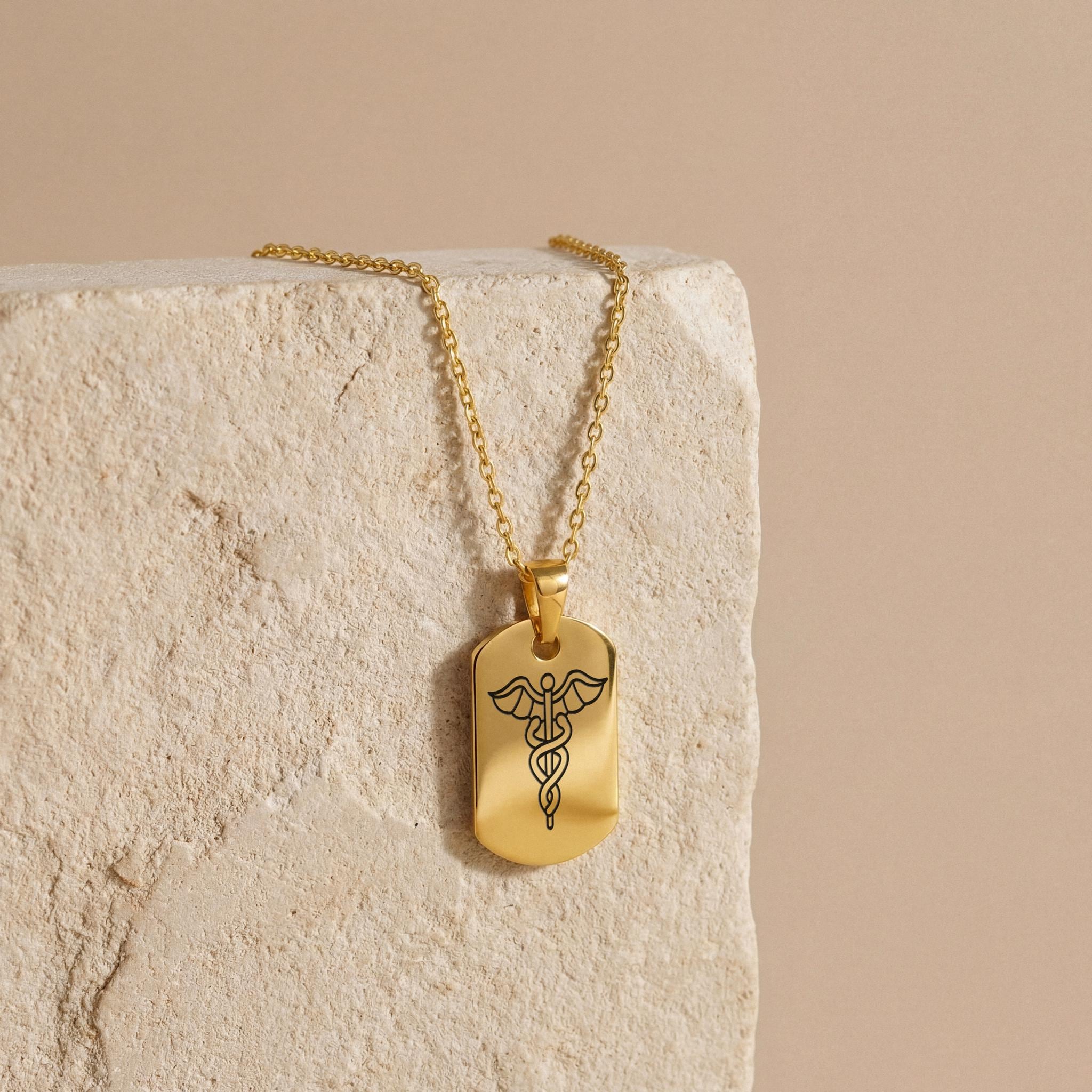 18K Gold Vermeil Personalized Medical ID Necklace with caduceus symbol engraving hanging on textured stone background.