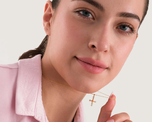 Woman wearing a gold necklace with a cross pendant against a plain background