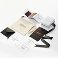 This image displays an array of packaging materials and printed items from "Mionza." Visible items include branded boxes, a pouch, ribbon, business cards, an envelope, a receipt, a thank you card featuring a Bow Ring design in 14K Solid Gold and a booklet—all with a sleek and professional aesthetic.