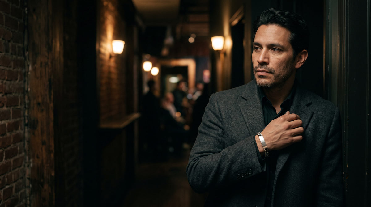 Man in a dark suit in a lit New York alley wearing a silver cuff bracelet