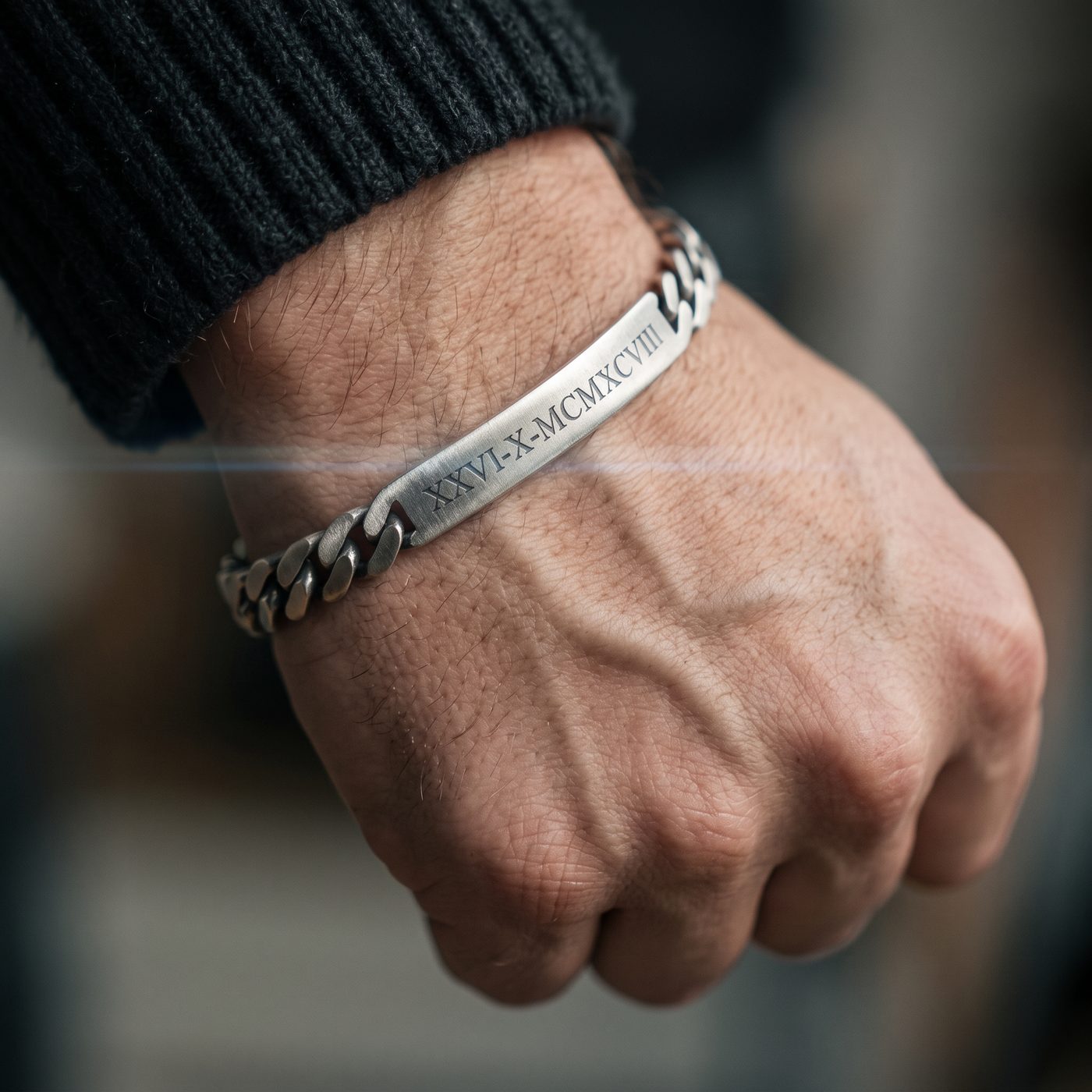 Close-up of a silver curb chain ID bracelet engraved with Roman numerals on a man's wrist