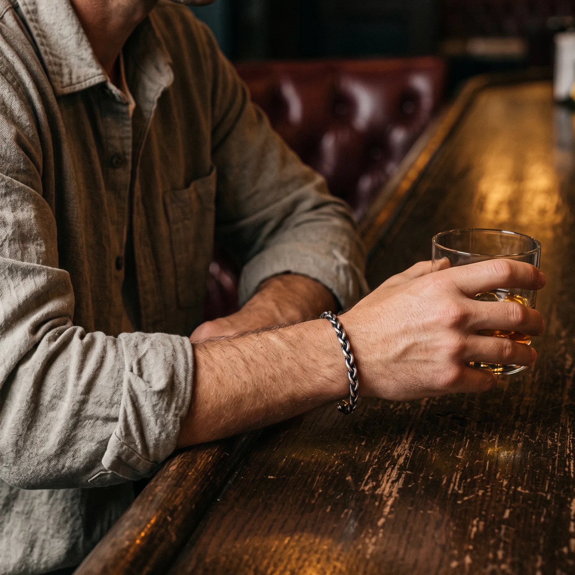 Man at a wooden bar with a whiskey wearing a silver chain bracelet