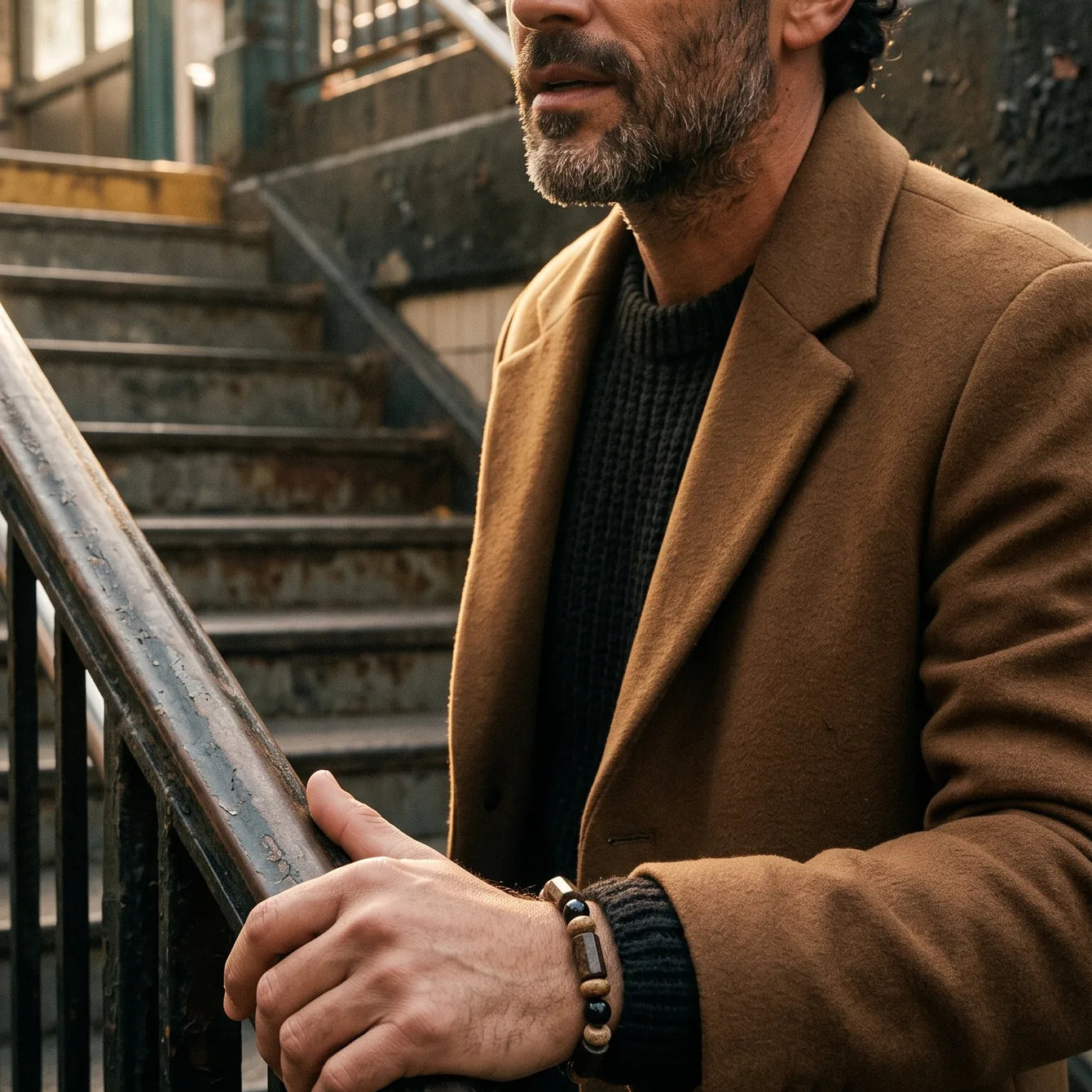 Man in a camel coat on subway stairs wearing a bracelet