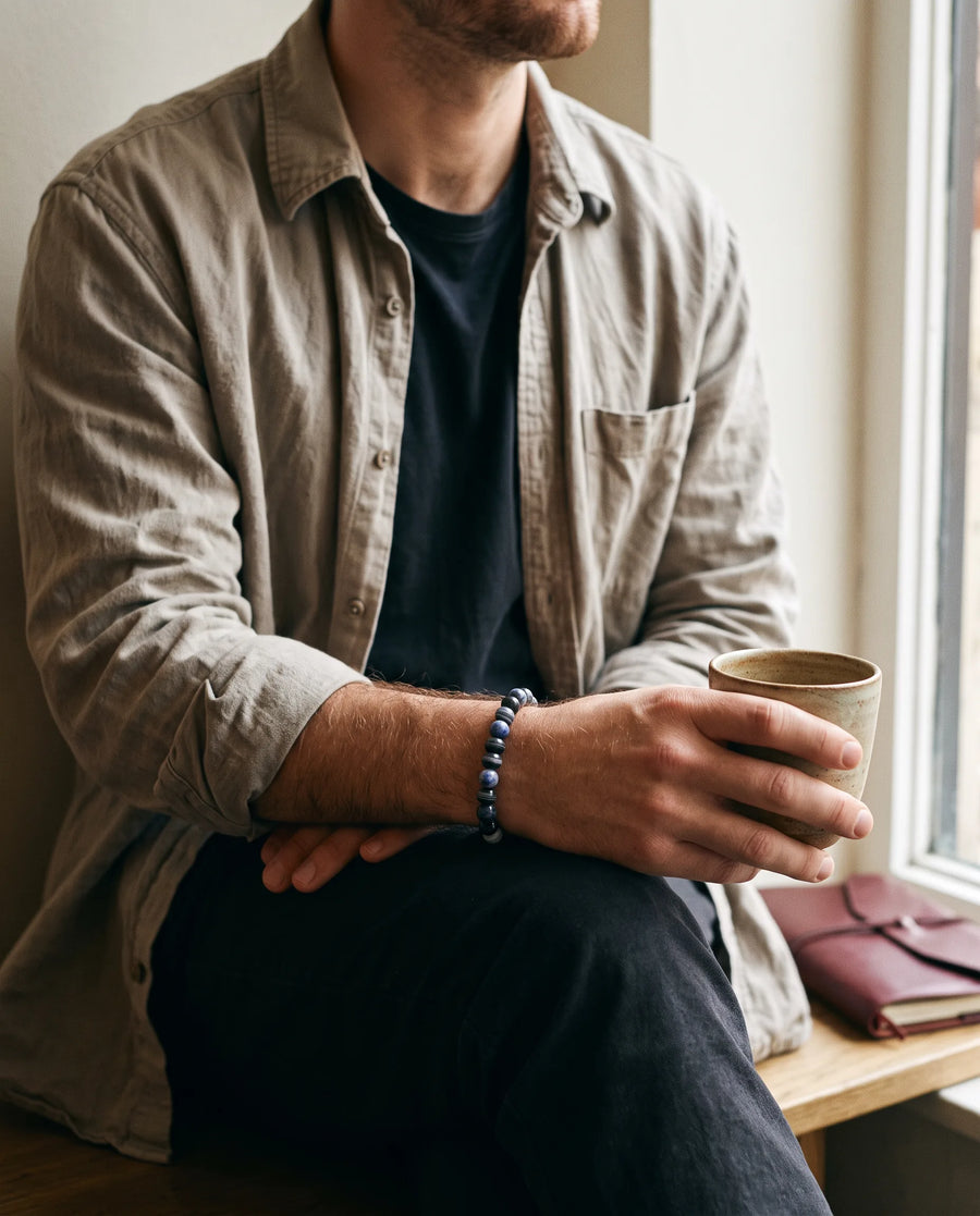 Man in a linen shirt at a cafe window wearing a sodalite bracelet