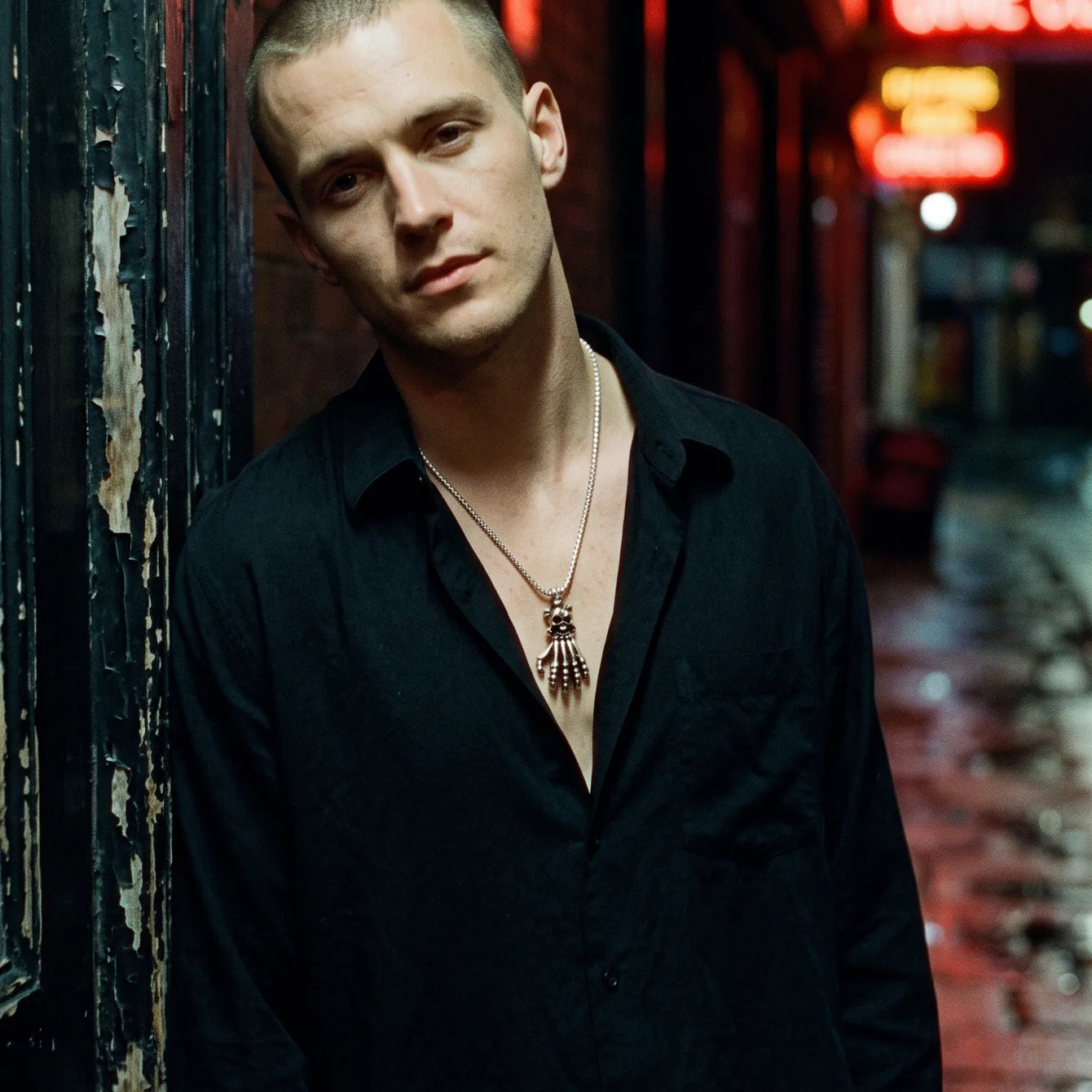 Man in a neon-lit alley wearing a skeleton hand necklace