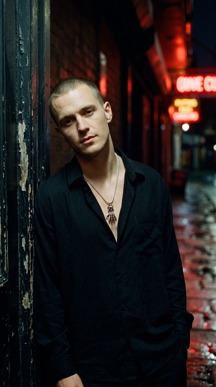 Man in a neon-lit alley wearing a skeleton hand necklace