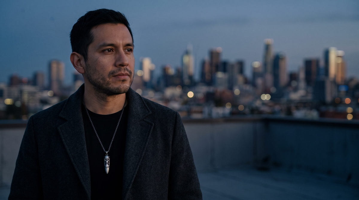 Man on a rooftop at dusk above the New York skyline wearing a silver pendant necklace