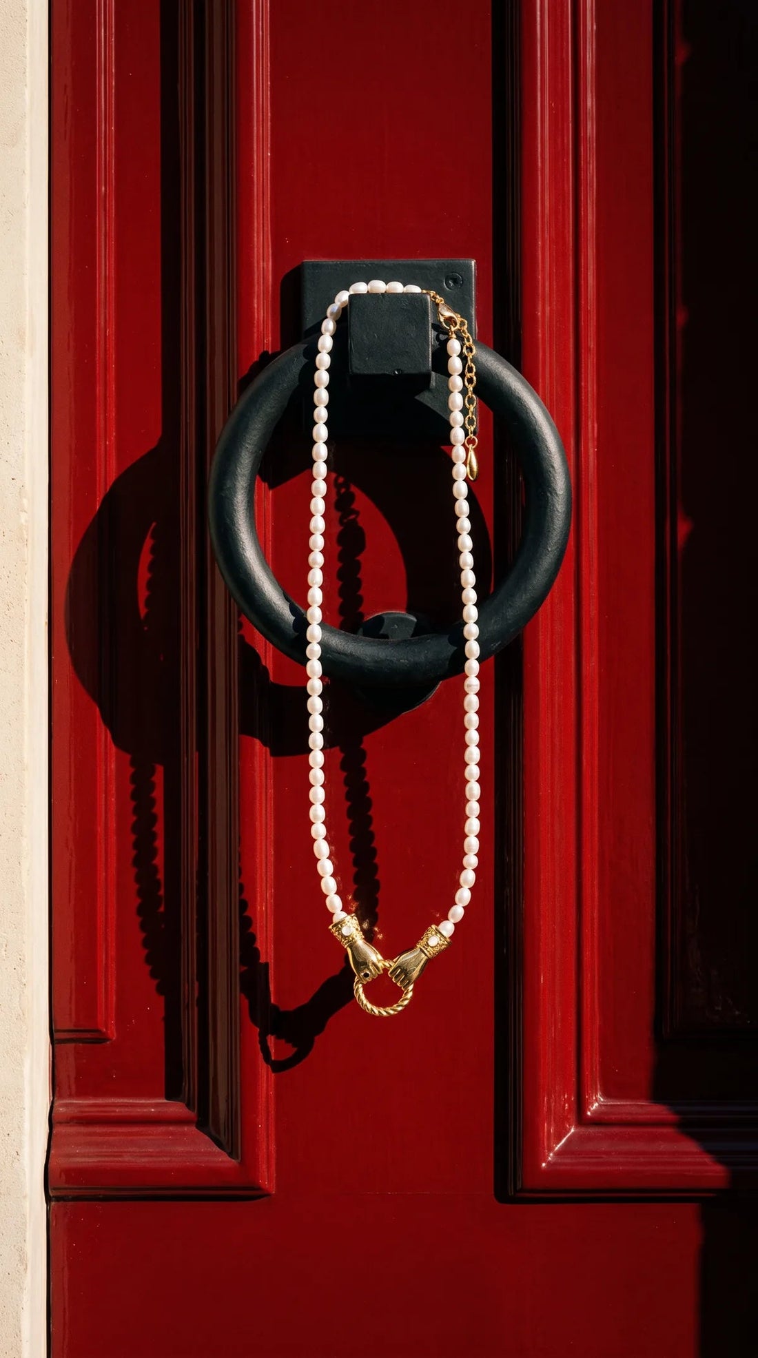 Holding hands pearl necklace on a red door knocker