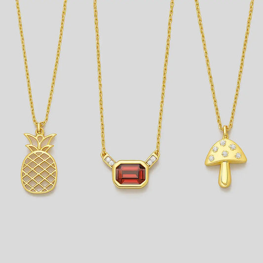 Three gold necklaces with pineapple, gemstone, and mushroom pendants on a light gray background.