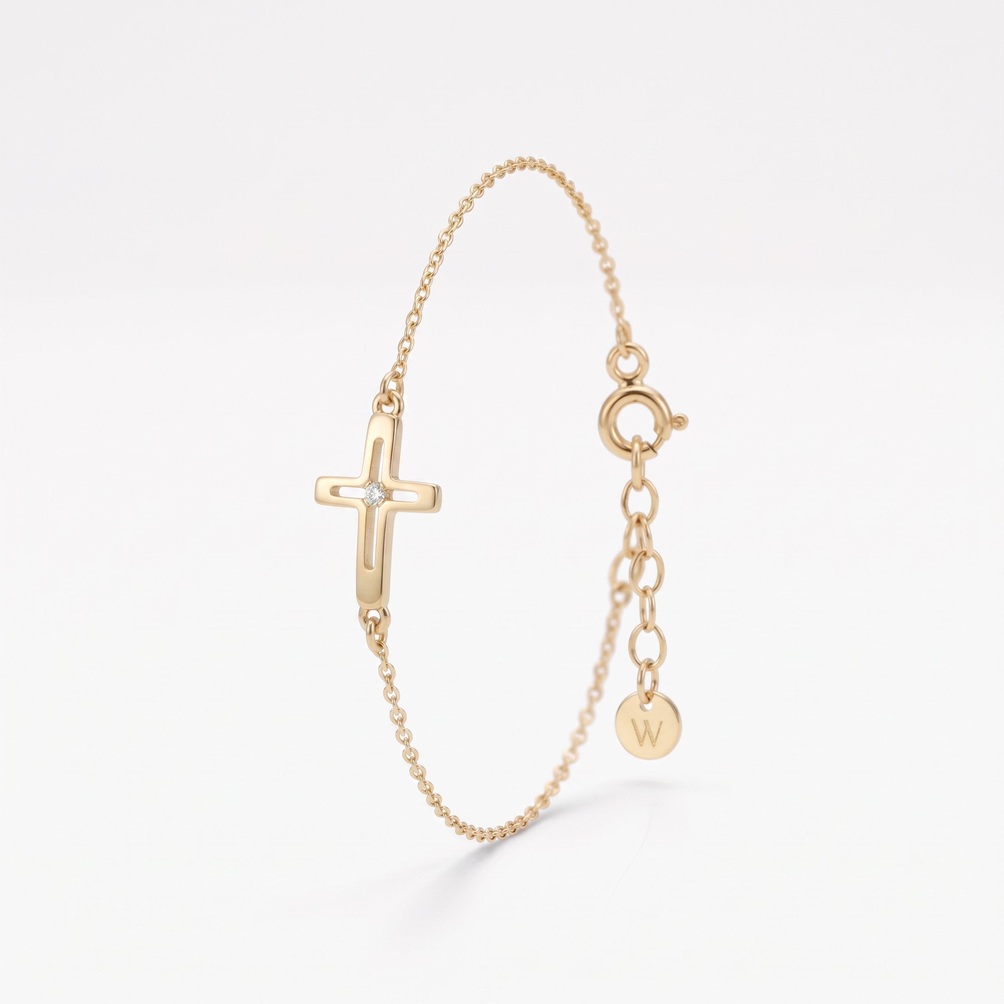 Gold sideways cross bracelet for women, an open cross with a single sparkling center stone on a dainty chain with extender
