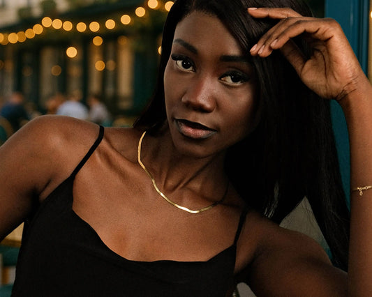 Woman wearing a black top and gold necklace with blurred lights in the background